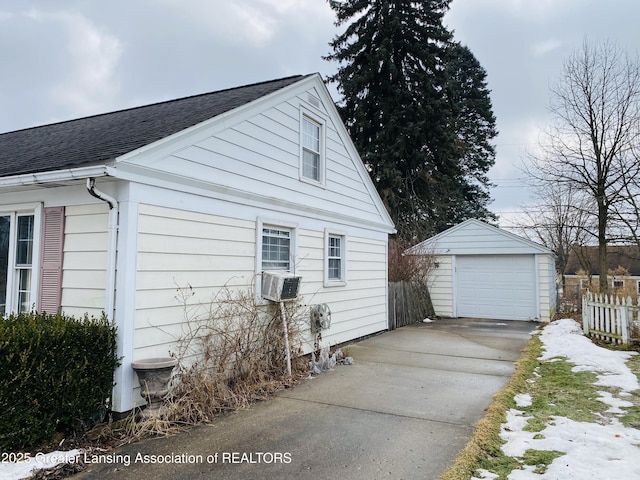 view of side of property featuring driveway, a shingled roof, a detached garage, an outbuilding, and fence