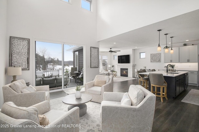 living room featuring a towering ceiling, ceiling fan, dark wood-type flooring, a fireplace, and recessed lighting