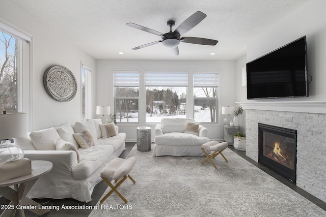 living area featuring a stone fireplace, a healthy amount of sunlight, a textured ceiling, and ceiling fan