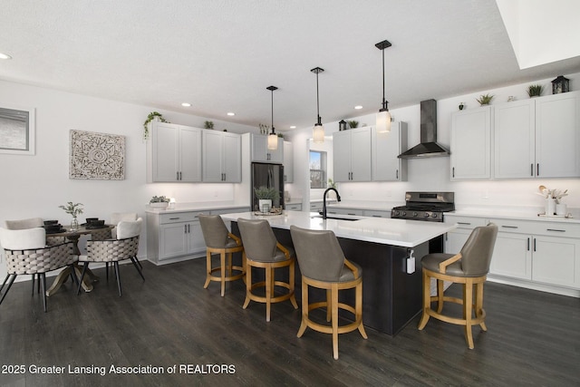 kitchen featuring gas stove, wall chimney range hood, a kitchen breakfast bar, and fridge