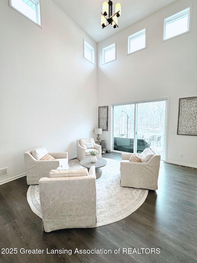 living area with dark wood-type flooring, a towering ceiling, baseboards, and an inviting chandelier