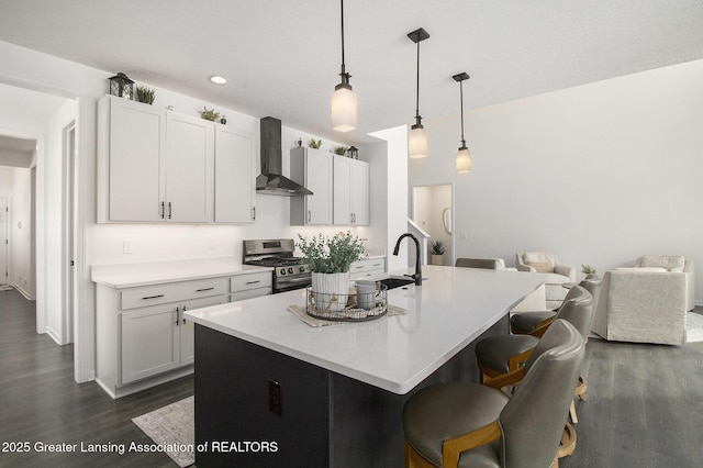 kitchen featuring wall chimney exhaust hood, dark wood-type flooring, gas stove, and a sink