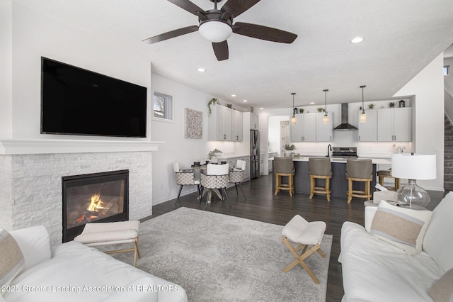 living area featuring ceiling fan, a fireplace, dark wood finished floors, and recessed lighting