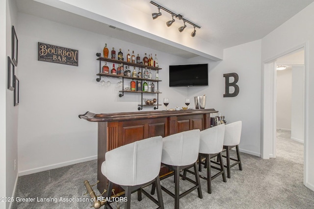 bar featuring rail lighting, baseboards, light colored carpet, and a dry bar