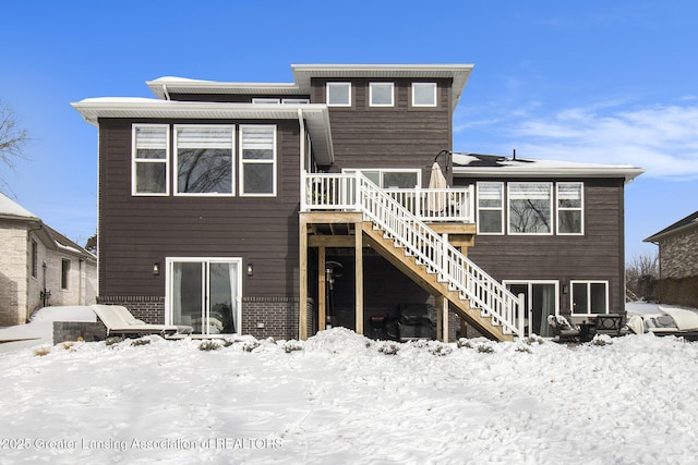 snow covered house featuring brick siding, stairs, and a wooden deck