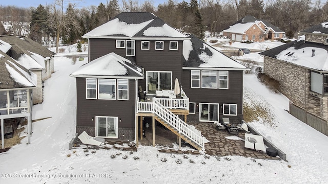 snow covered back of property with a patio area, stairway, and a deck