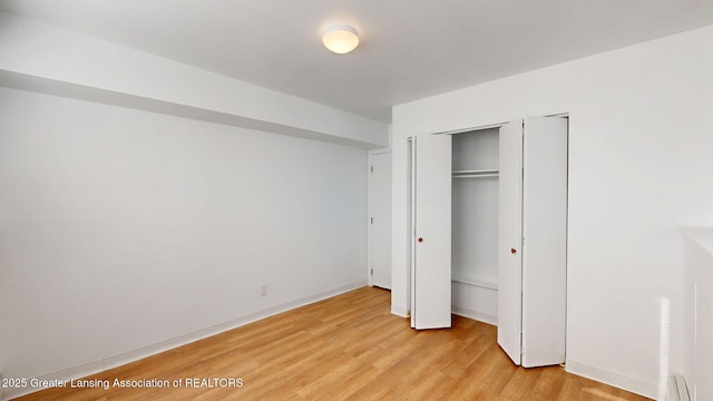 unfurnished bedroom with a baseboard heating unit and light wood-style floors