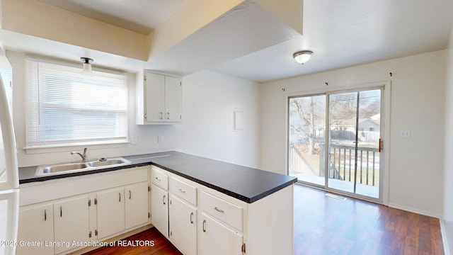 kitchen featuring a peninsula, dark countertops, dark wood finished floors, and a sink