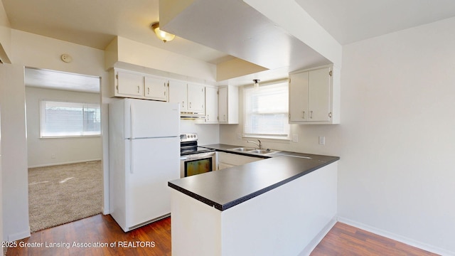 kitchen with freestanding refrigerator, a peninsula, stainless steel range with electric cooktop, white cabinetry, and a sink