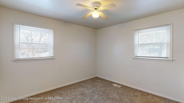 carpeted spare room featuring a ceiling fan, visible vents, plenty of natural light, and baseboards