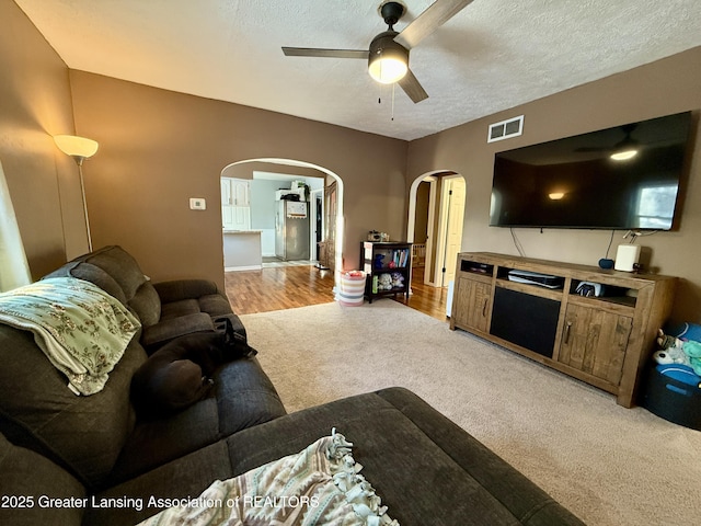 carpeted living room featuring ceiling fan, visible vents, arched walkways, and a textured ceiling