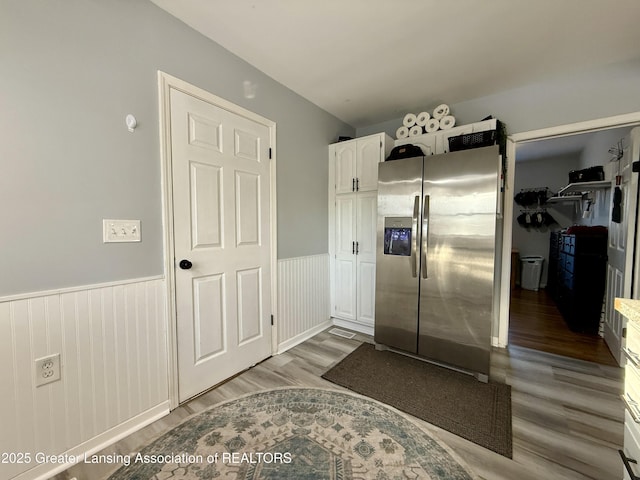 kitchen featuring a wainscoted wall, wood finished floors, stainless steel fridge, and white cabinetry