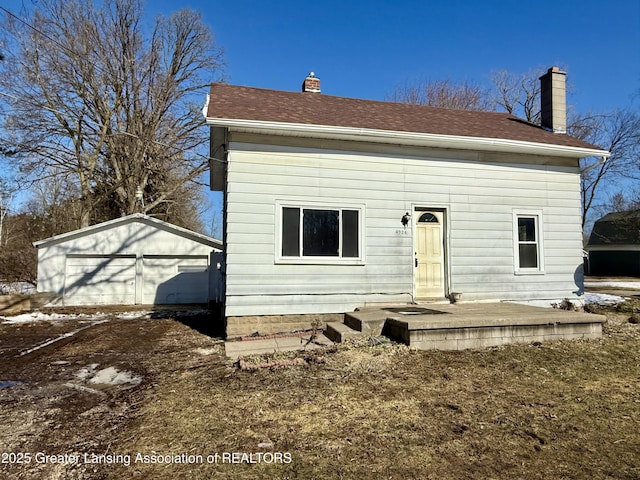 back of house featuring an outbuilding, roof with shingles, and a chimney