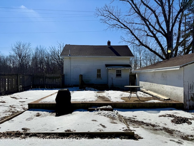 snow covered property with a chimney and fence