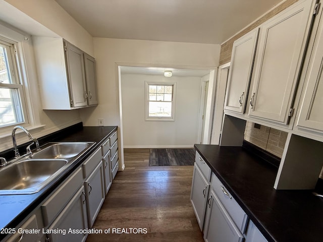 kitchen featuring a sink, baseboards, dark wood-style floors, tasteful backsplash, and dark countertops