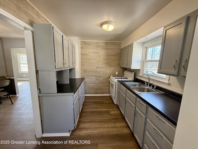 kitchen with plenty of natural light, dark countertops, white range with gas stovetop, and a sink