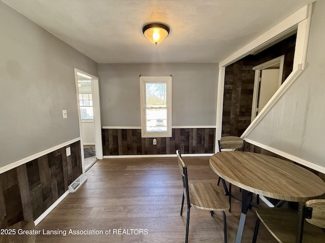 dining space featuring wainscoting, wood walls, visible vents, and wood finished floors