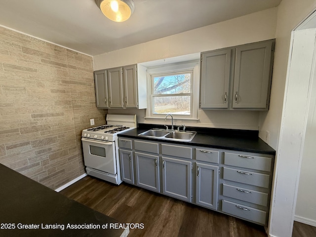 kitchen with dark countertops, a sink, gray cabinetry, and white gas range oven