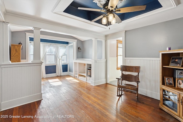 living area with a tray ceiling, decorative columns, wainscoting, ceiling fan, and hardwood / wood-style flooring