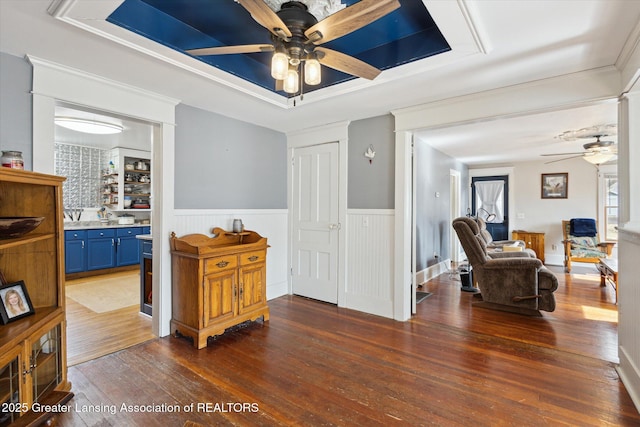 interior space with a wainscoted wall, ornamental molding, a raised ceiling, and hardwood / wood-style floors