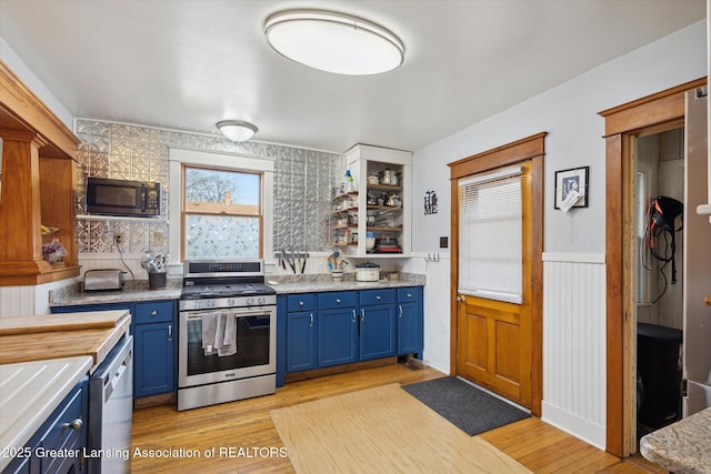 kitchen with a wainscoted wall, light wood-style flooring, blue cabinets, stainless steel gas range, and black microwave