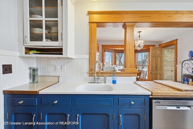 kitchen with a wainscoted wall, stainless steel dishwasher, a sink, blue cabinets, and ornate columns