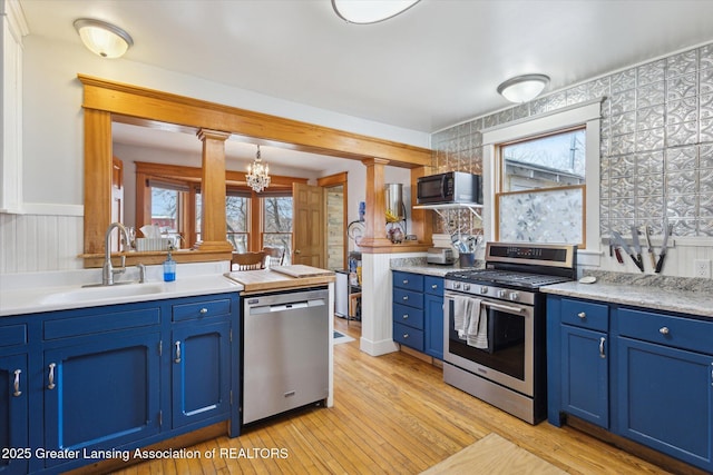 kitchen featuring stainless steel appliances, a sink, light countertops, blue cabinetry, and light wood finished floors