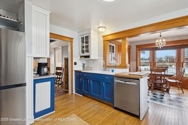 kitchen with light wood finished floors, blue cabinets, stainless steel appliances, white cabinetry, and a sink