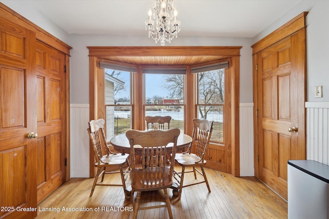 dining space with a chandelier, a wainscoted wall, and light wood-style floors