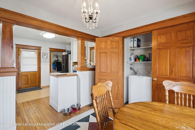 dining area with washer / dryer, decorative columns, light wood finished floors, and an inviting chandelier