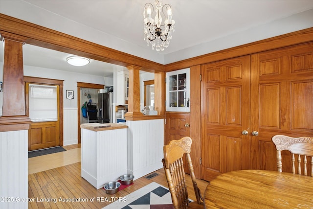 dining area with decorative columns, visible vents, a wainscoted wall, light wood-style flooring, and a notable chandelier