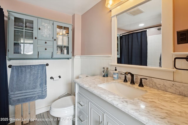 bathroom featuring a wainscoted wall, curtained shower, visible vents, toilet, and vanity