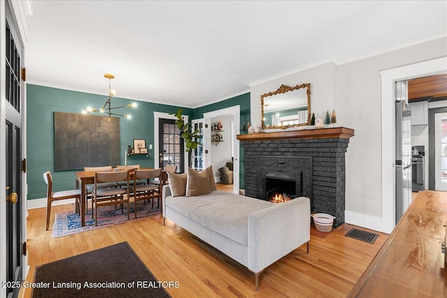 living area featuring light wood finished floors, baseboards, visible vents, ornamental molding, and a fireplace