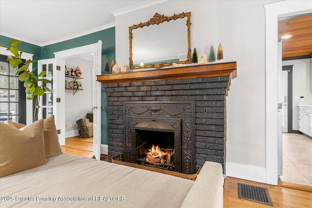 living room featuring crown molding, a fireplace, visible vents, wood finished floors, and baseboards