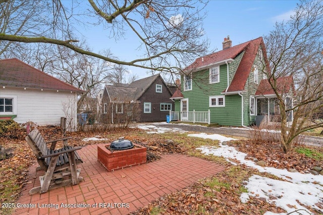 rear view of property with a chimney, a patio area, a fire pit, and roof with shingles