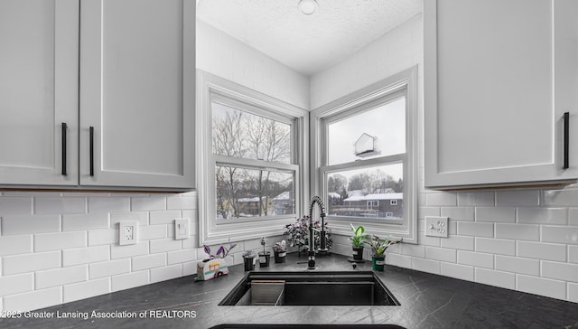 kitchen featuring tasteful backsplash, dark countertops, a sink, and a textured ceiling