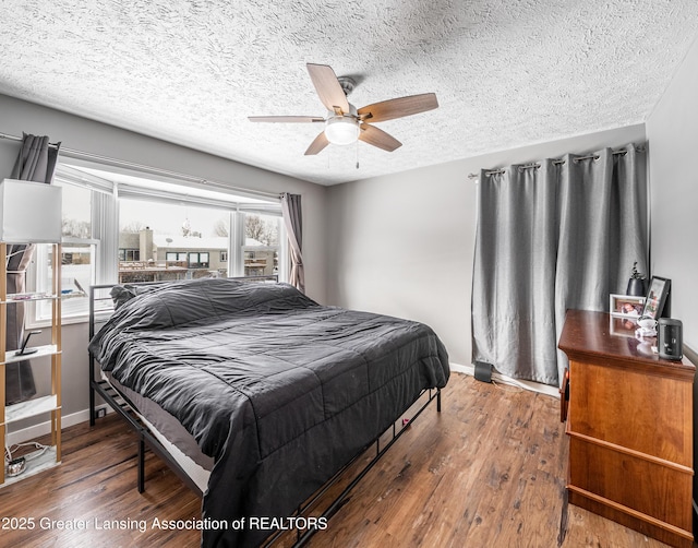 bedroom with ceiling fan, a textured ceiling, baseboards, and wood finished floors