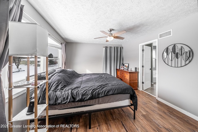 bedroom featuring baseboards, visible vents, a ceiling fan, wood finished floors, and a textured ceiling