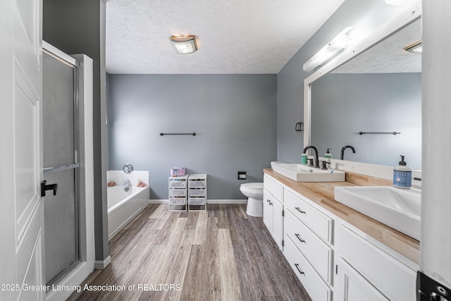 full bathroom with a stall shower, double vanity, a sink, and wood finished floors