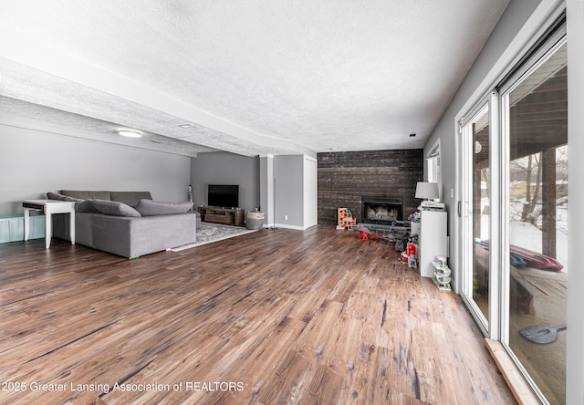 unfurnished living room featuring a large fireplace, a textured ceiling, baseboards, and wood finished floors