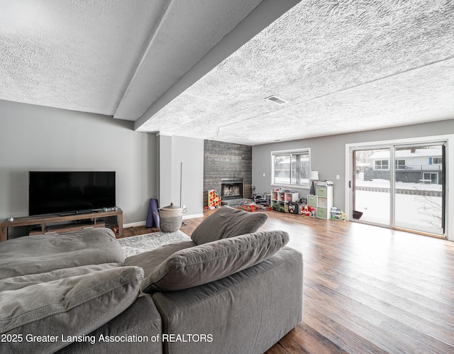 living area featuring a large fireplace, visible vents, baseboards, wood finished floors, and a textured ceiling