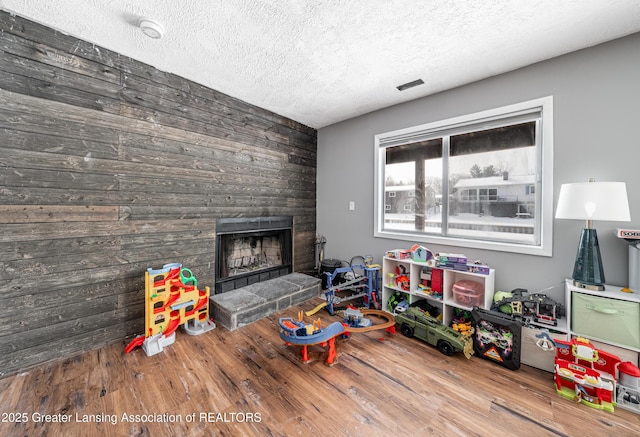 game room with a textured ceiling, visible vents, wood finished floors, and a stone fireplace