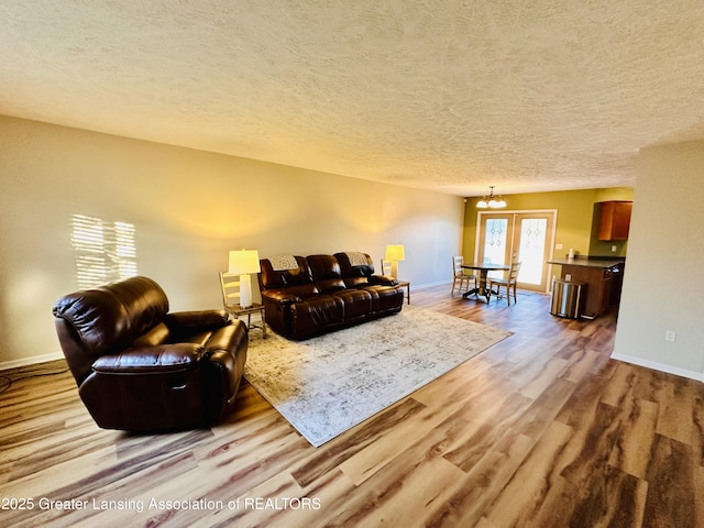 living room featuring a textured ceiling, an inviting chandelier, wood finished floors, and baseboards