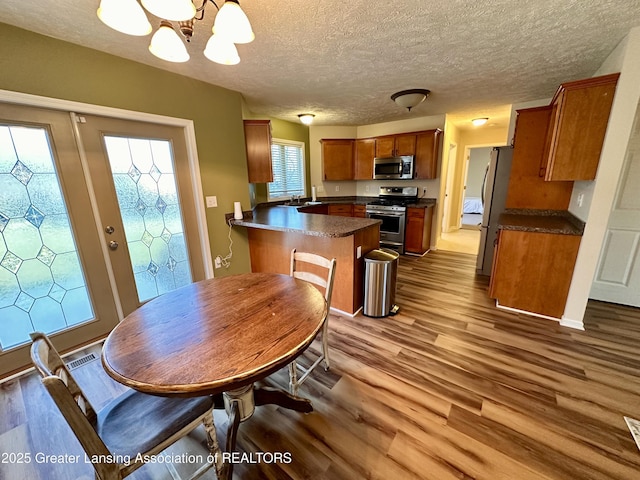 kitchen with dark countertops, appliances with stainless steel finishes, brown cabinetry, wood finished floors, and a peninsula