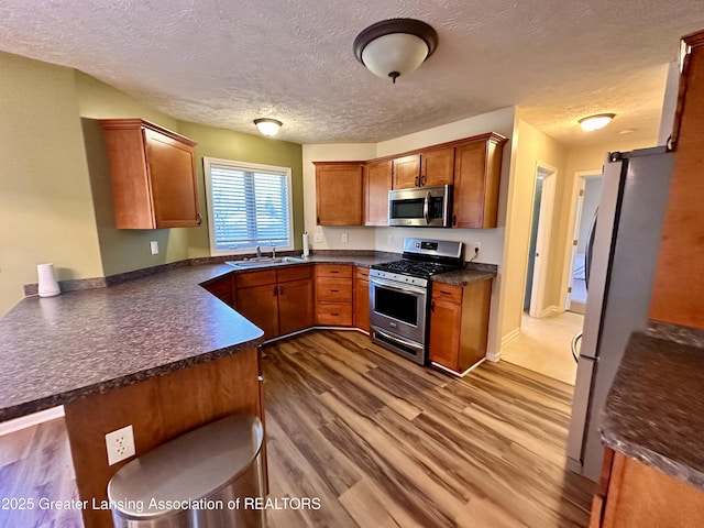 kitchen with stainless steel appliances, a peninsula, wood finished floors, a sink, and dark countertops