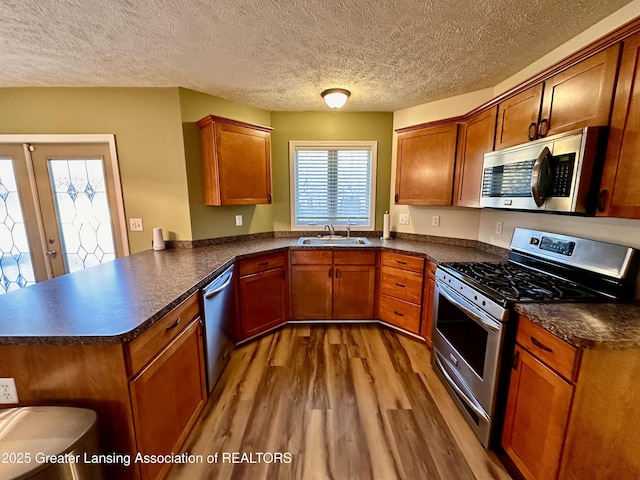 kitchen with dark countertops, appliances with stainless steel finishes, a peninsula, light wood-style floors, and a sink