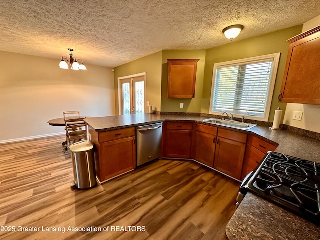 kitchen featuring dark countertops, a sink, gas range, dishwasher, and a peninsula