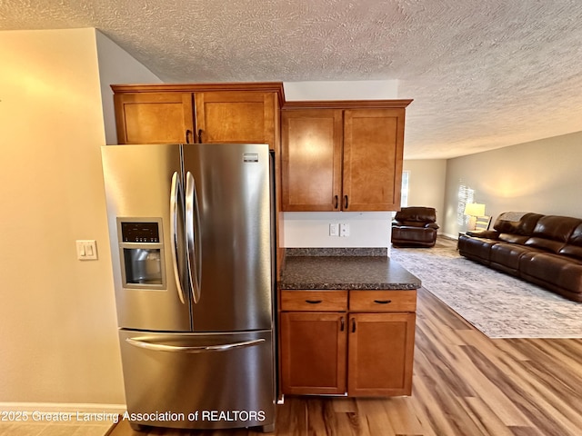 kitchen featuring dark countertops, brown cabinetry, open floor plan, wood finished floors, and stainless steel fridge