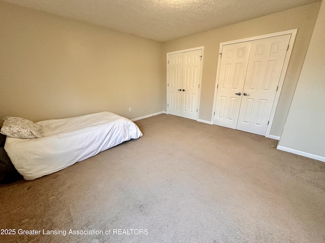 bedroom with carpet floors, a textured ceiling, baseboards, and two closets