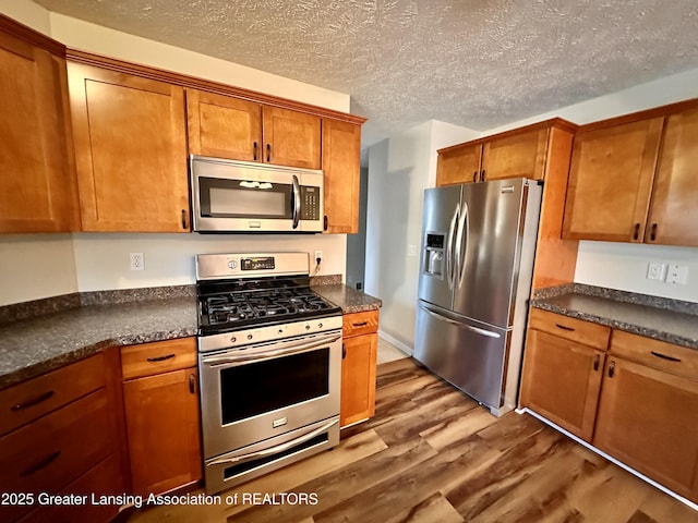 kitchen with brown cabinets, dark countertops, appliances with stainless steel finishes, a textured ceiling, and wood finished floors